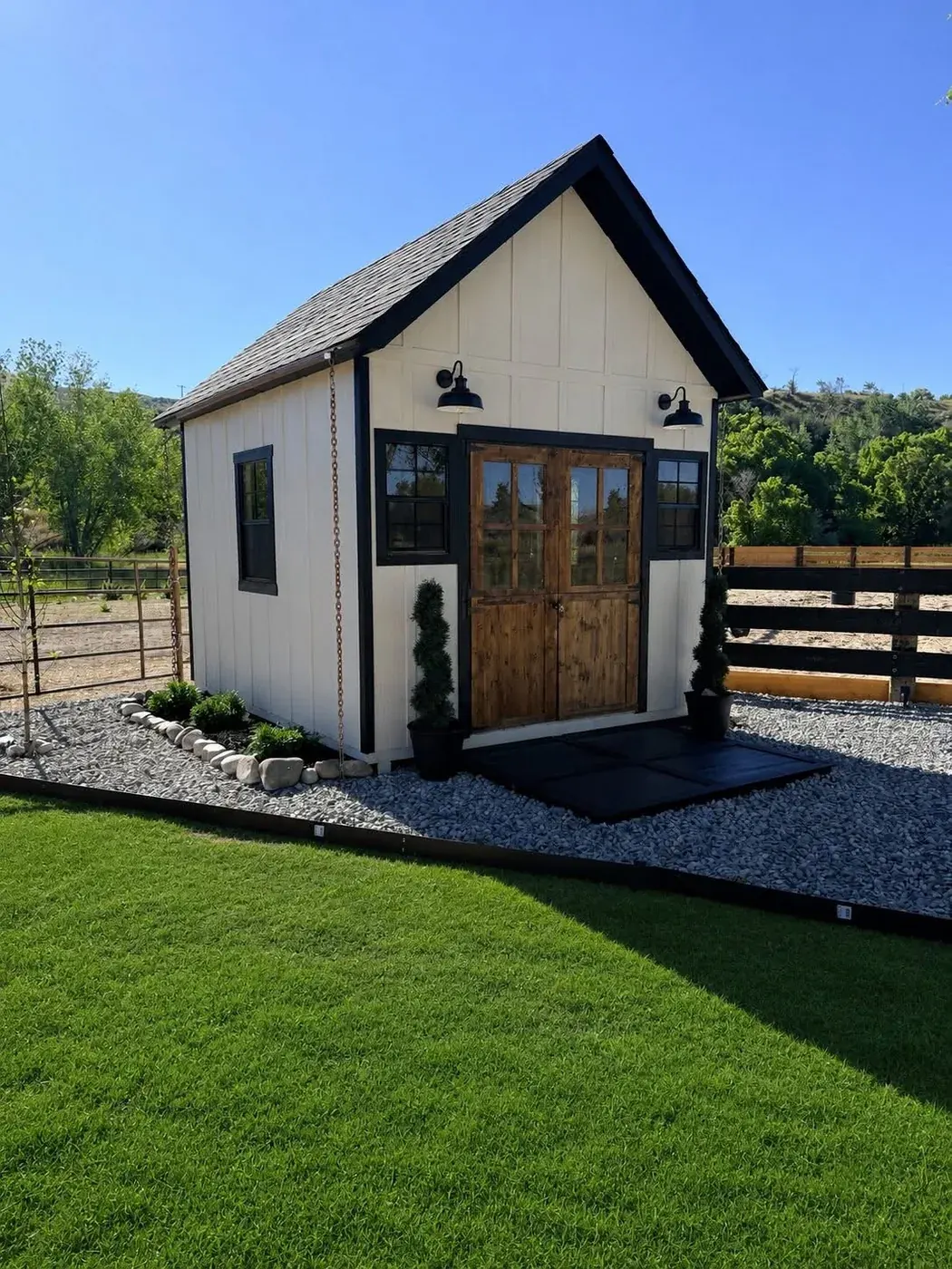 White board-and-batten cottage shed with a steep gable roof, cedar french doors, black trim and barn lights, built on-site by ShedPro LLC